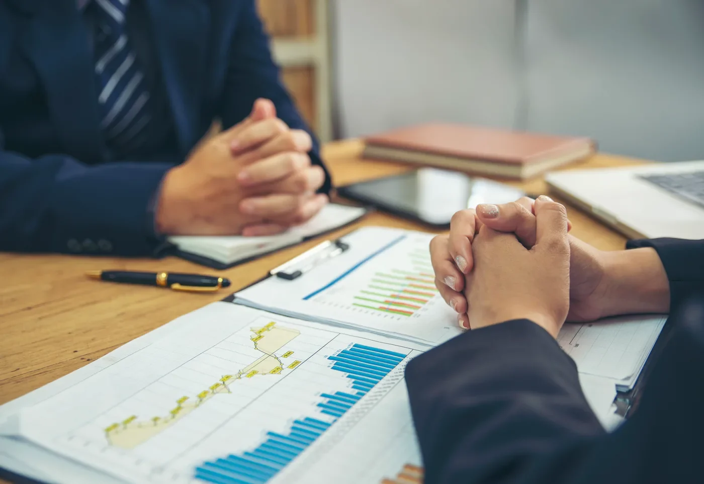 Değerleme görüşmesi: masada karşılıklı oturan iki taraf ile önlerinde duran finansal grafik ve tablolar.